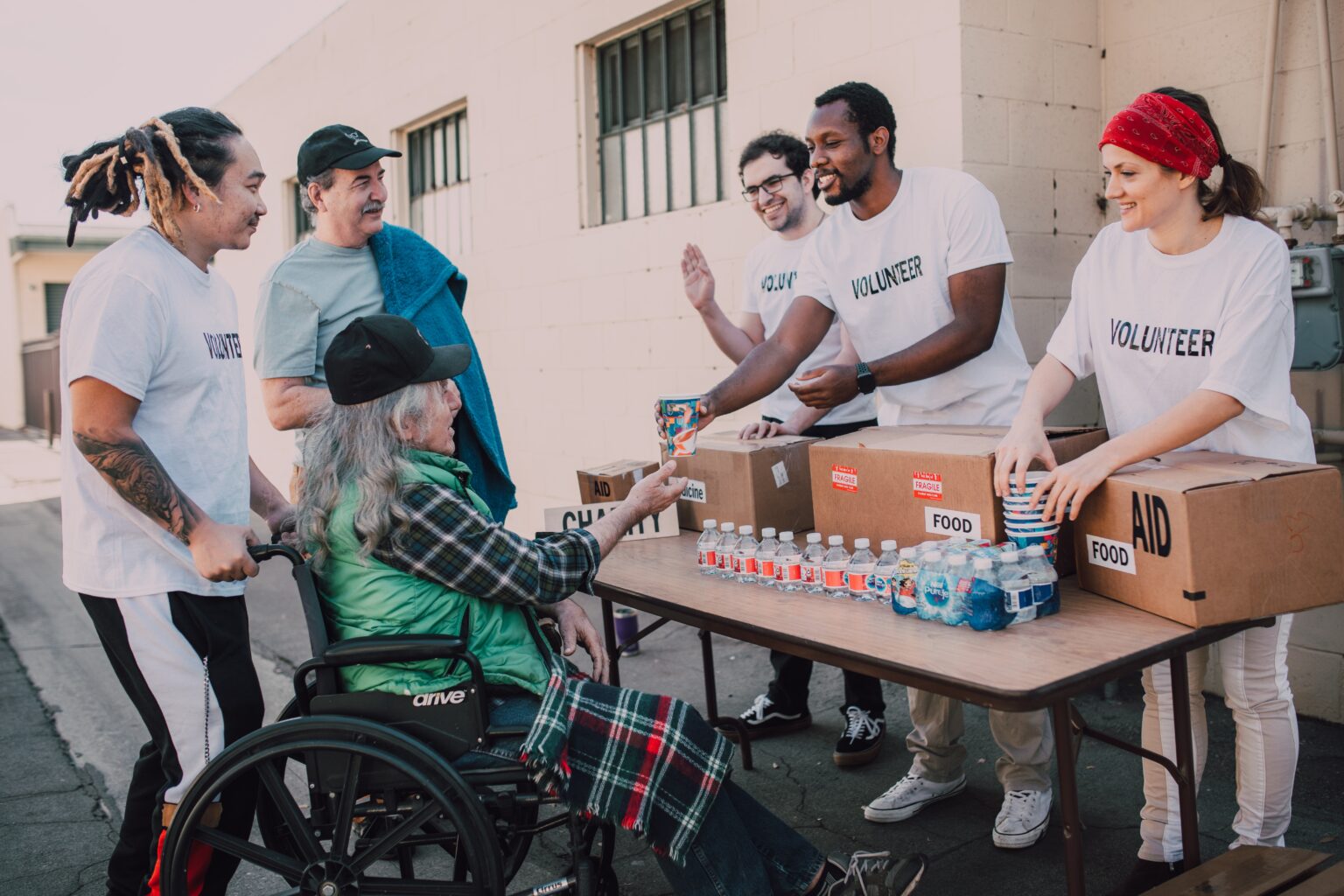 As part of a community program, volunteers distribute food and water to two elderly veterans.